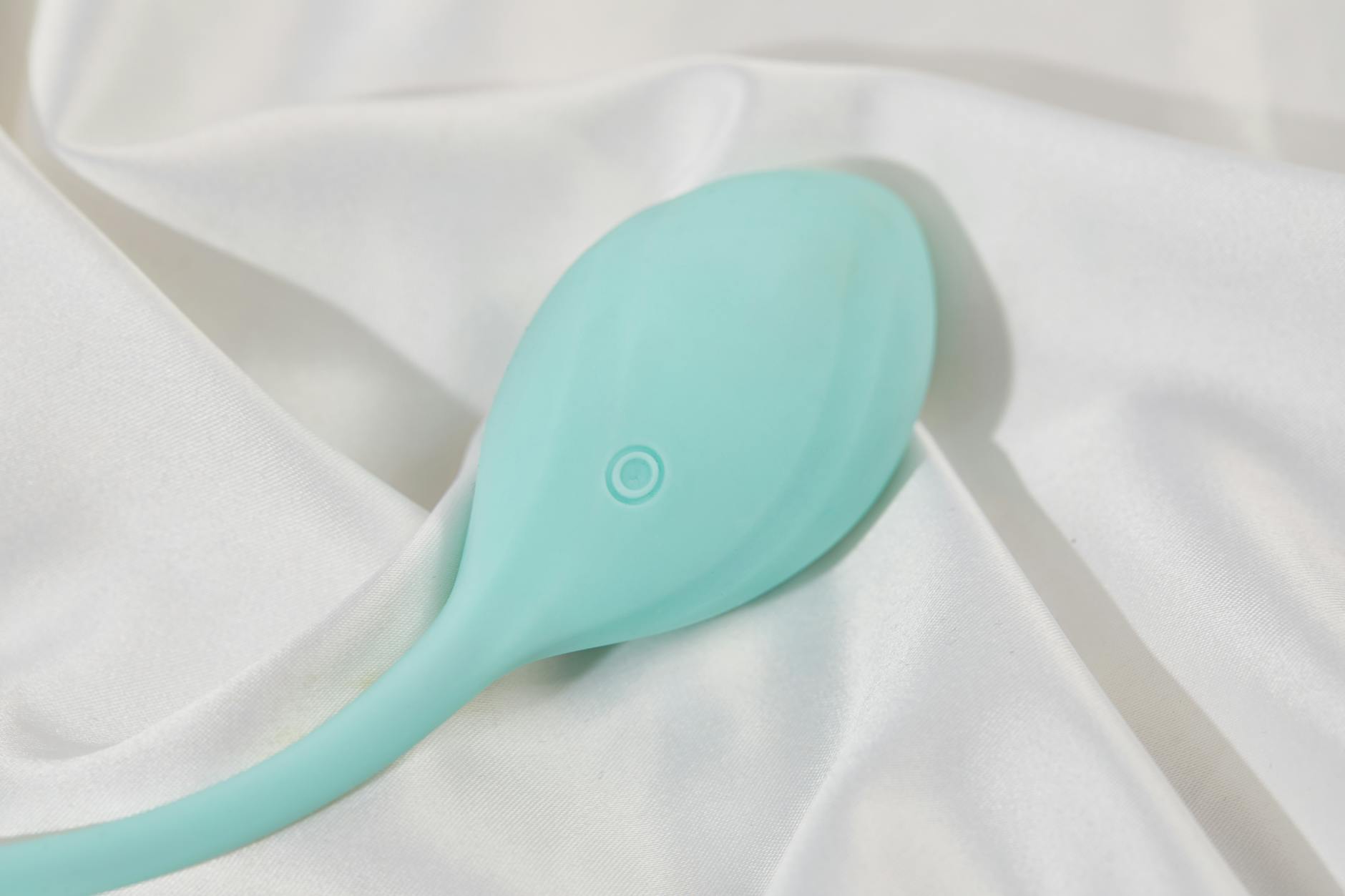 A teal lemon clitoral vibrator on soft white silk, ready for use