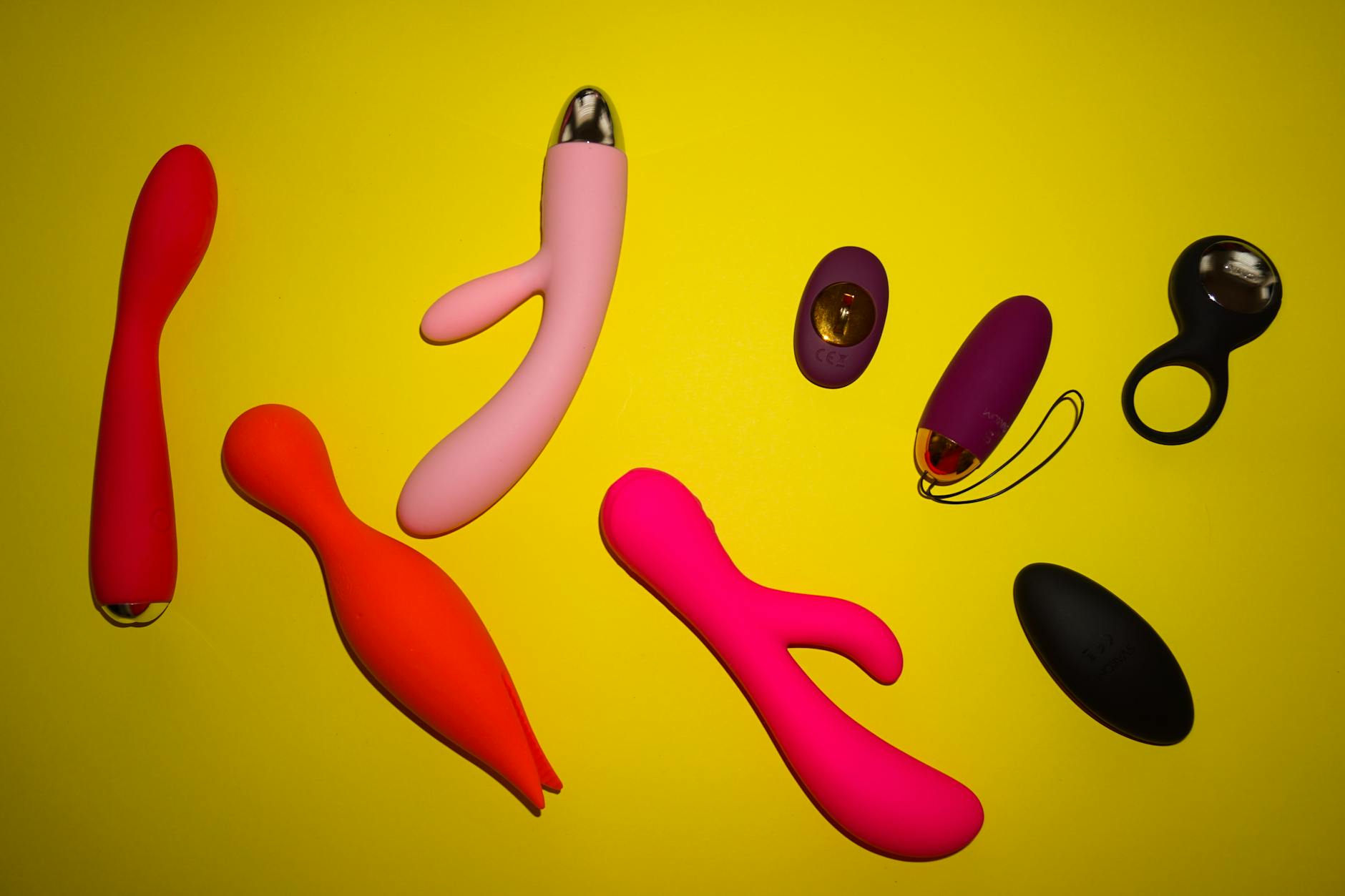 Vibrant arrangement of various colorful sex toys on a bright yellow surface, showcasing modern pleasure devices