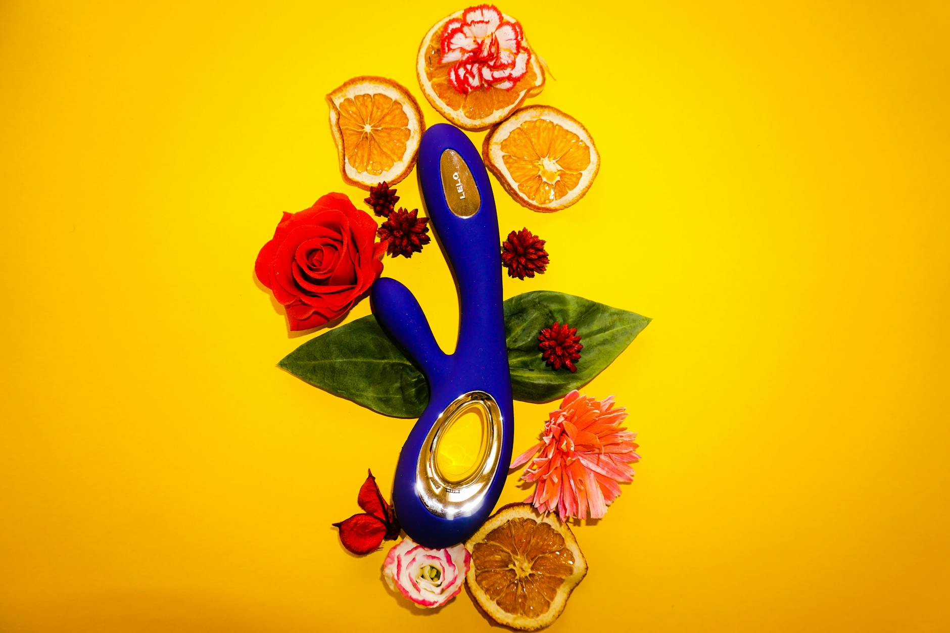 A lemon vibrator surrounded by fresh citrus and flowers on a yellow background, symbolizing renewed pleasure after menopause.
